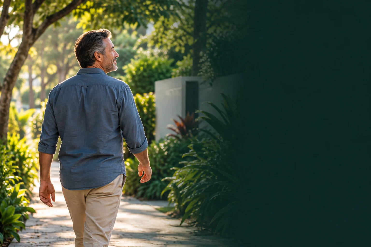 Hombre de mediana edad camina tranquilo y sonriente por un sendero arbolado, con luz natural de la mañana